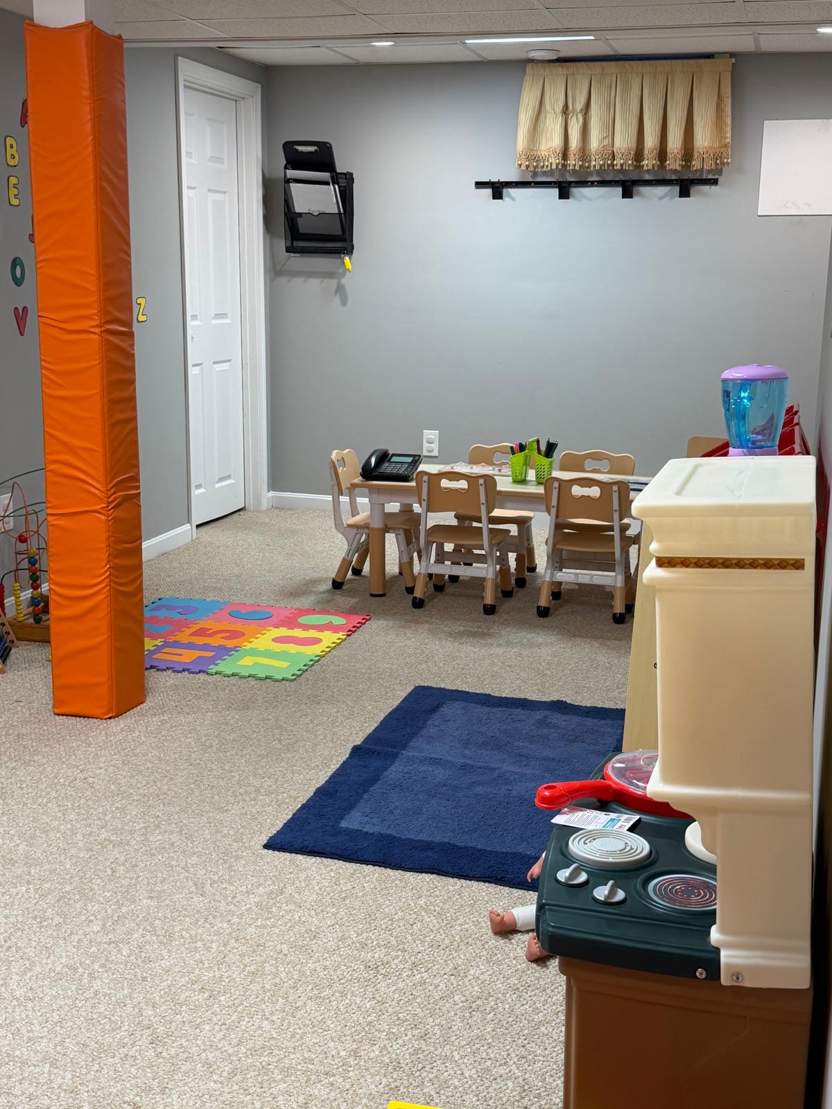 The orange feature wall with PLAY ALL DAY art, crayon border, licensing board, and reading nook