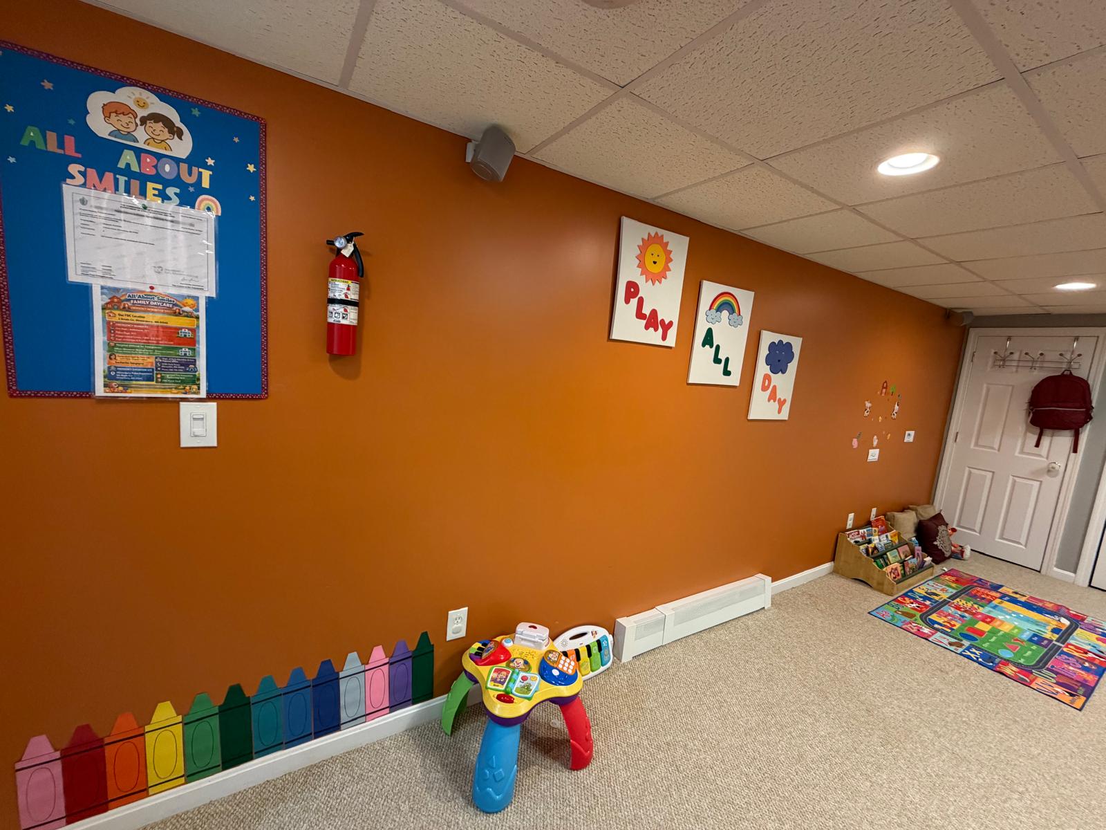 The activity room with the alphabet wall, child-sized table and chairs, and the orange play area beyond